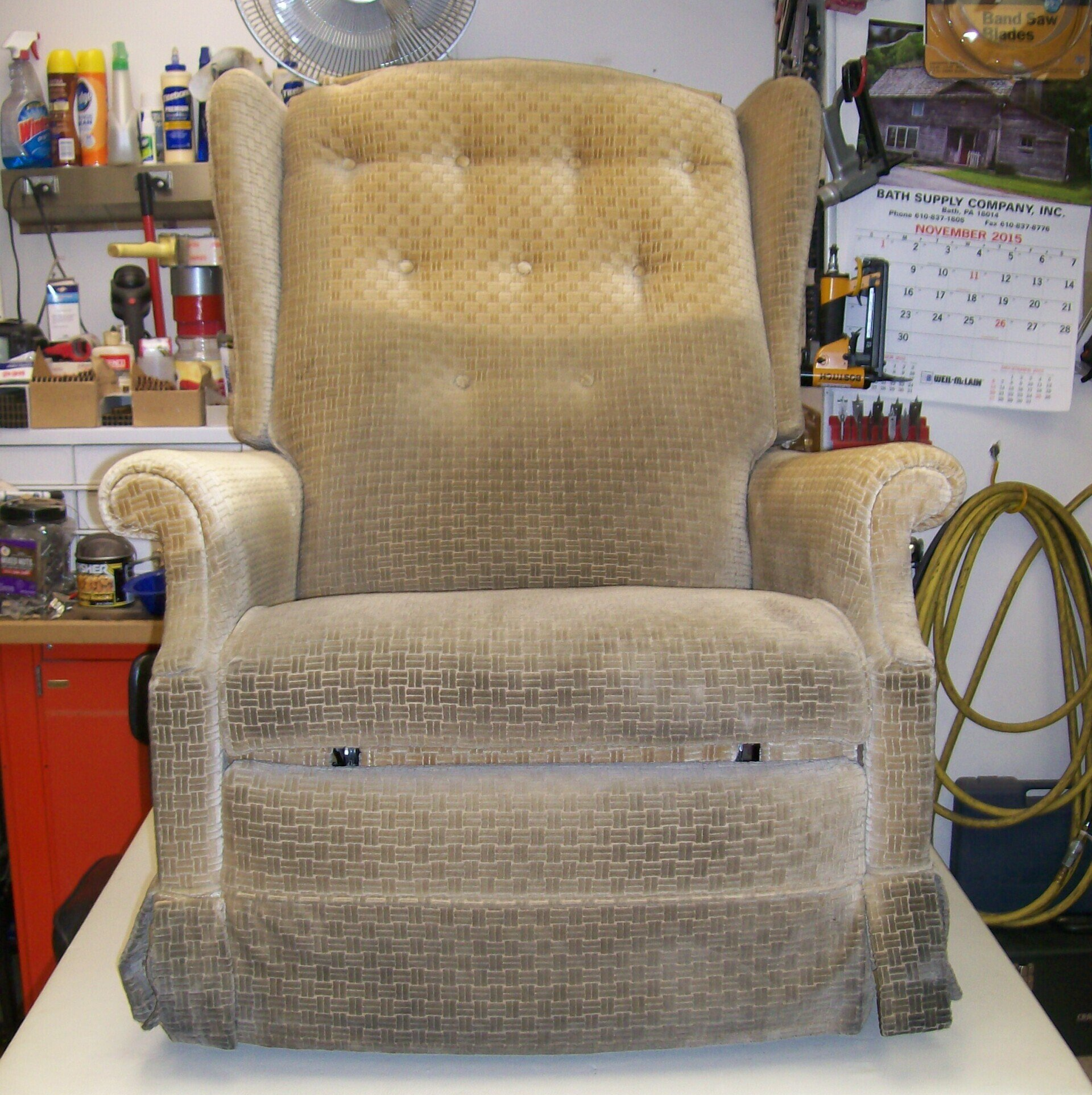 A tan recliner is sitting on a white table in front of a wall with a calendar on it