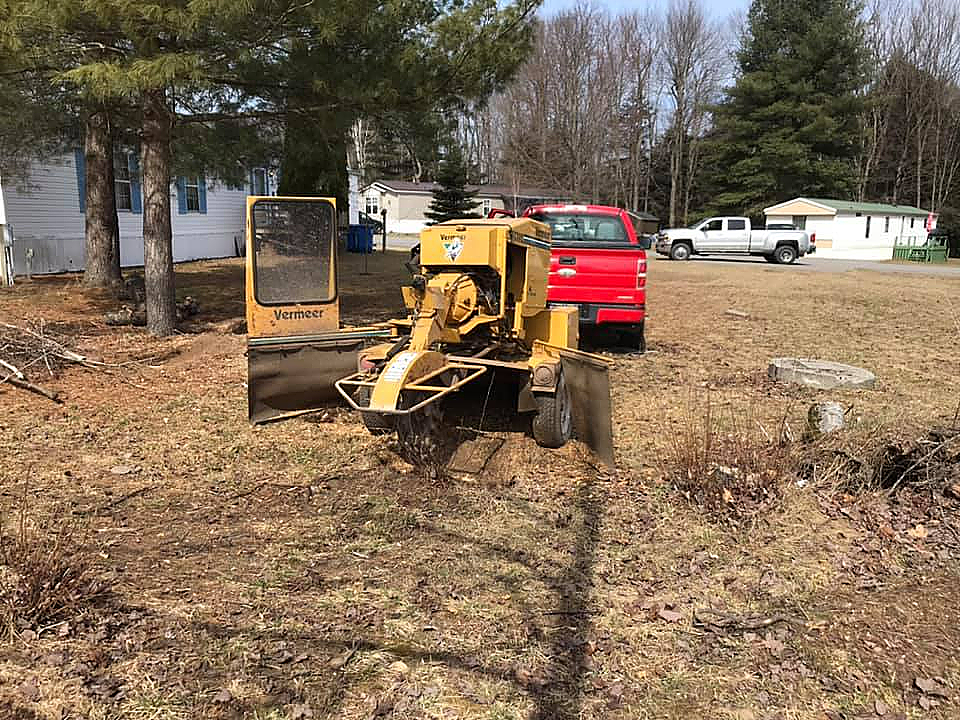 a yellow stump grinder is sitting in a field next to a red truck .