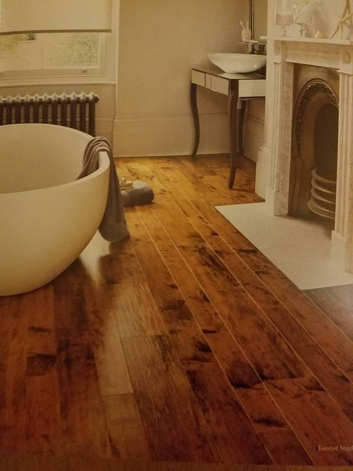 Bathroom with wood floor, white tub, antique fireplace, and vanity; warm lighting.