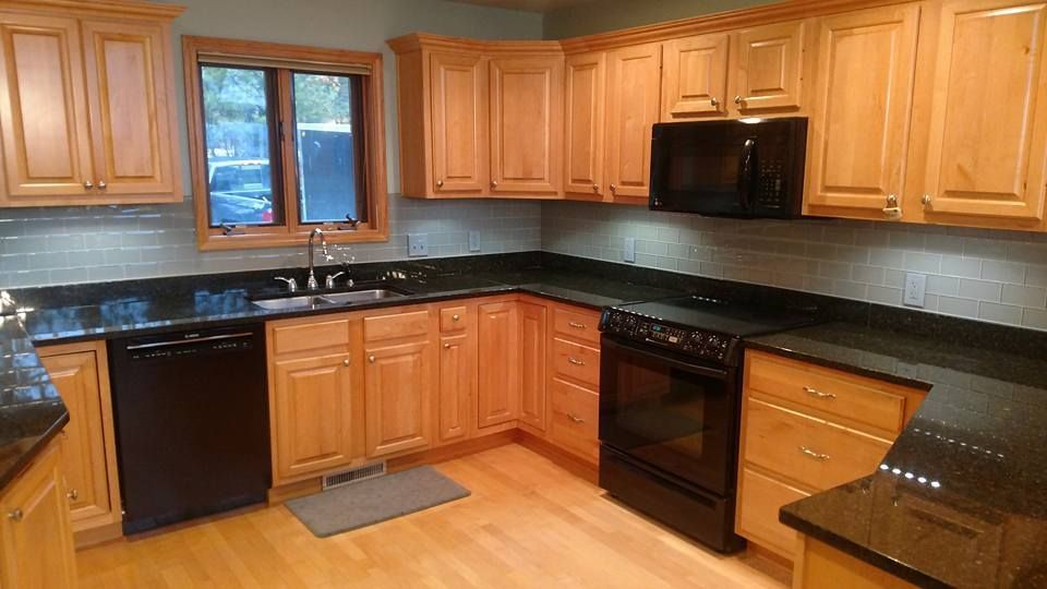 Kitchen with blonde cabinets, black appliances, and dark countertops.