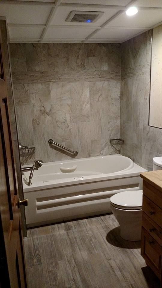 Bathroom with gray tile walls, white tub, wooden floor, and a toilet.