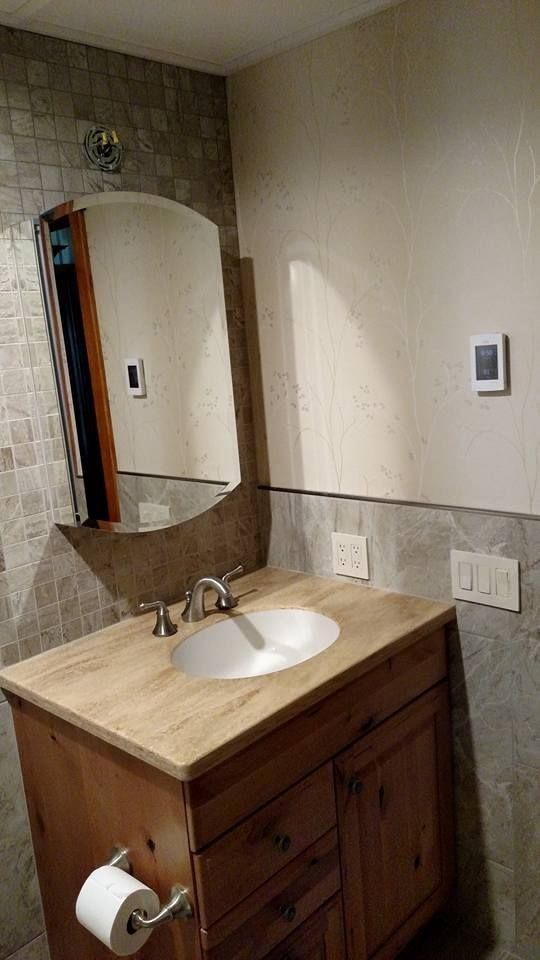 Bathroom vanity with a wooden cabinet, stone backsplash, and arched mirror.