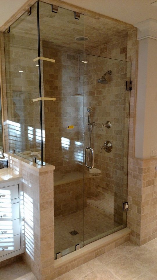 Glass-enclosed shower with beige tile walls, a built-in bench, and multiple showerheads.