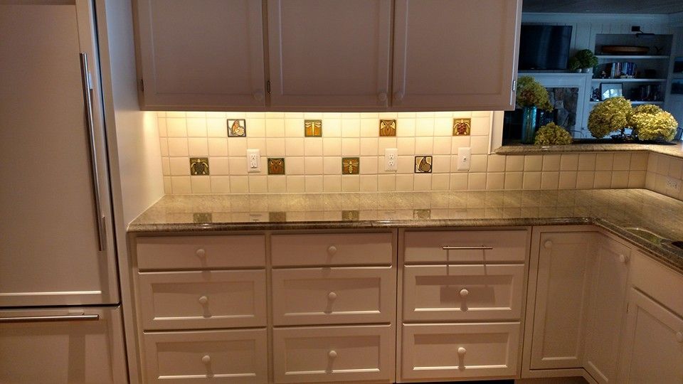 Cream-colored kitchen cabinets and granite countertops. Square decorative tiles on the backsplash.