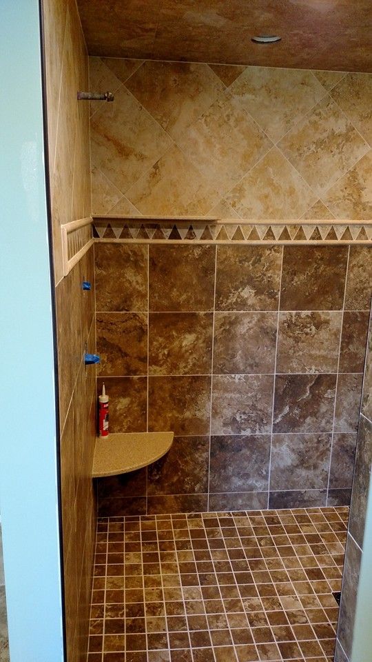 Tile-walled shower in warm brown tones, with a built-in bench and small patterned floor.