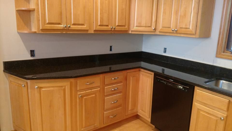Kitchen with light wood cabinets, black countertop, and a black dishwasher.