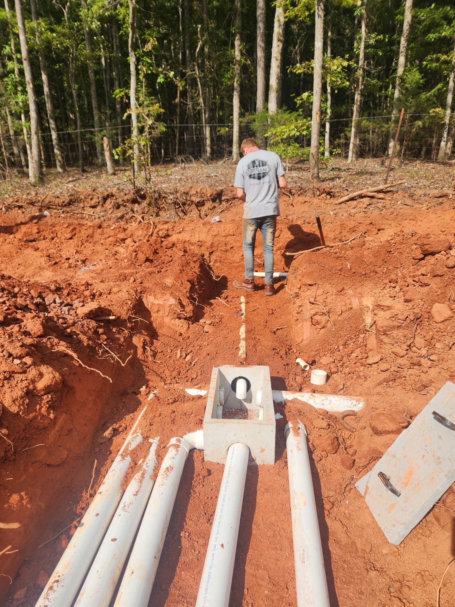 A man is standing in the dirt next to a row of white pipes