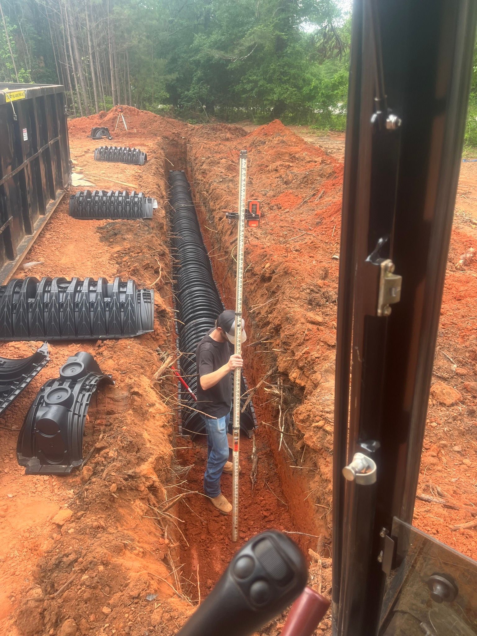 A man is standing in a trench holding a level