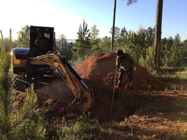 A man is digging a hole in the dirt in front of an excavator