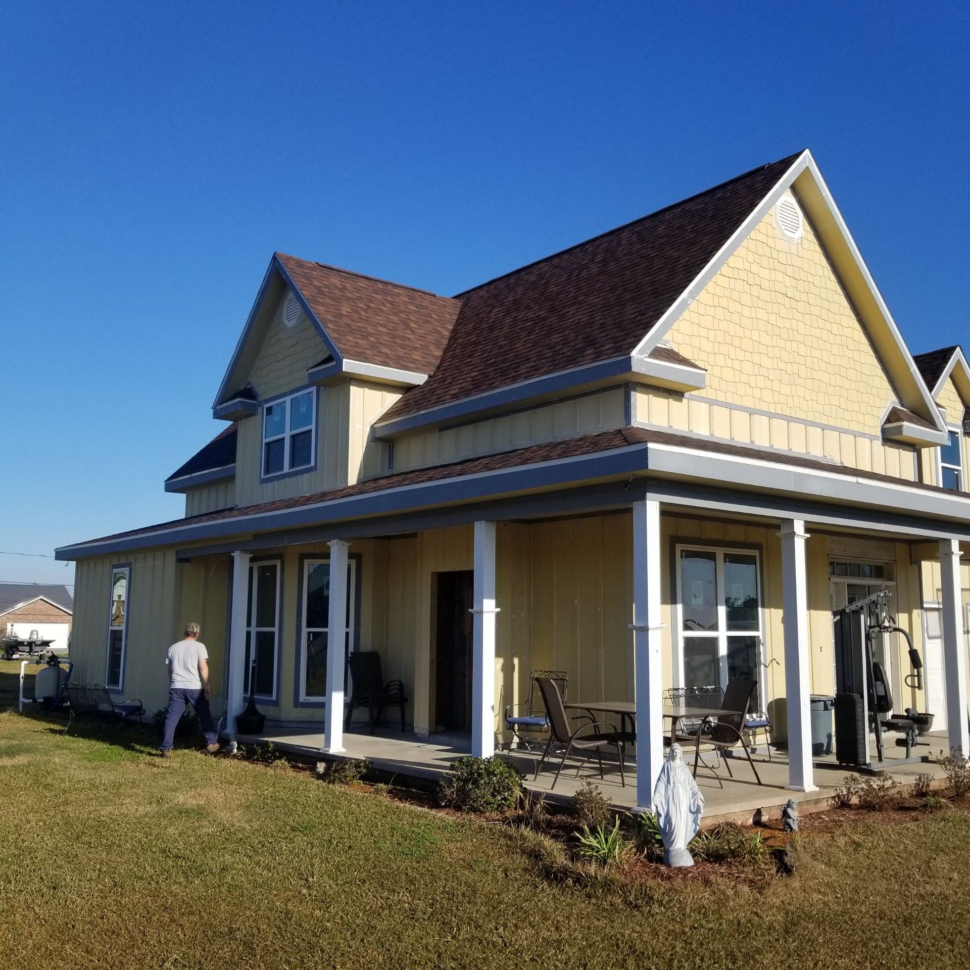 Yellow two-story house with porch. Person mowing lawn. Clear blue sky.