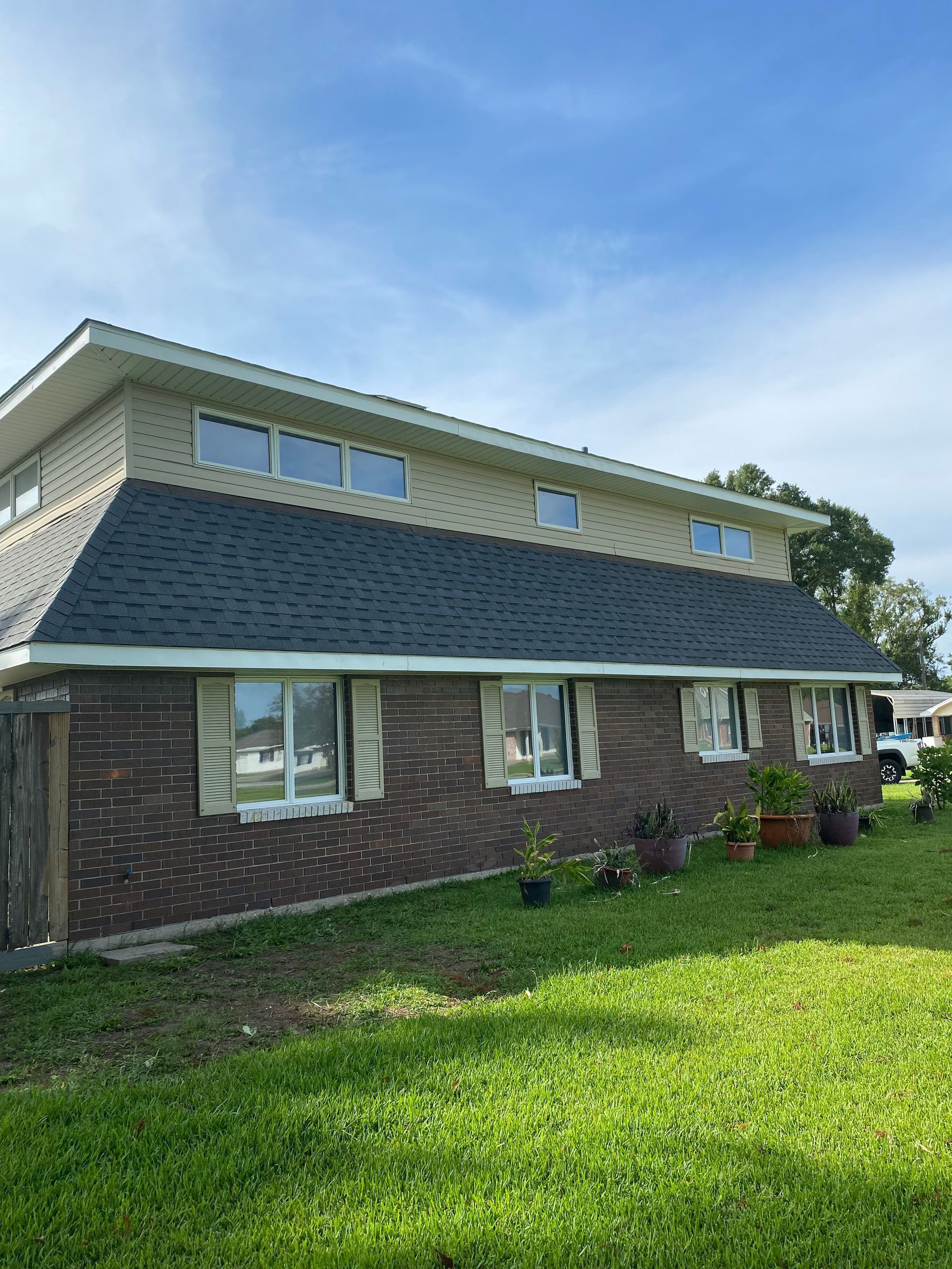 Two-story brick house with a dark roof and tan siding under a blue sky.