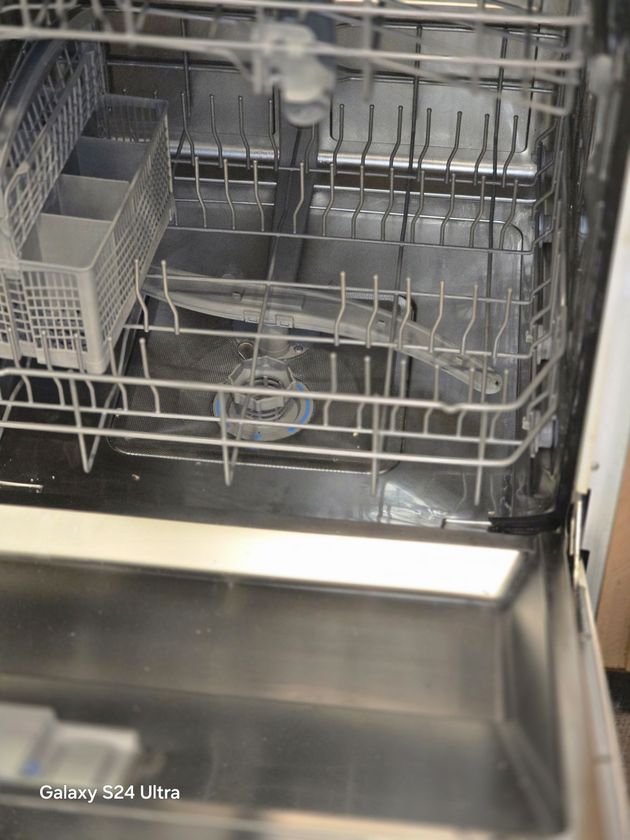 Open dishwasher with racks and utensils inside, metal interior visible