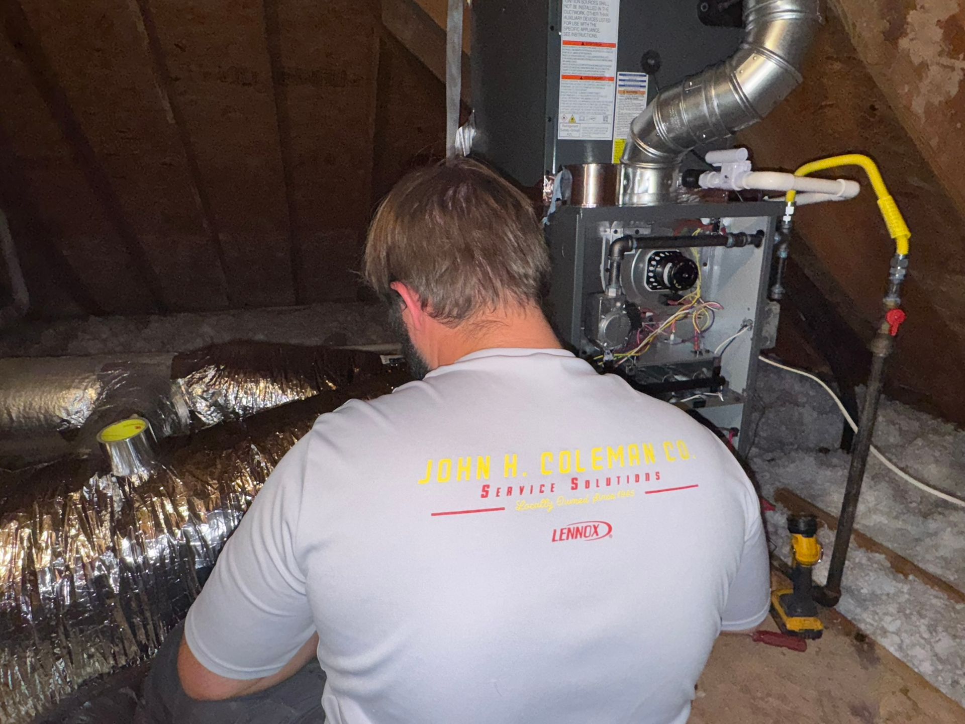 A person in a yellow hard hat tests electrical wiring inside a metal box.
