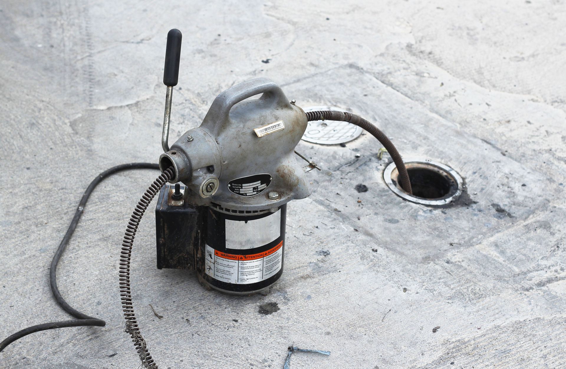 A drain cleaning machine with a cable inserted into a drain opening set in concrete.