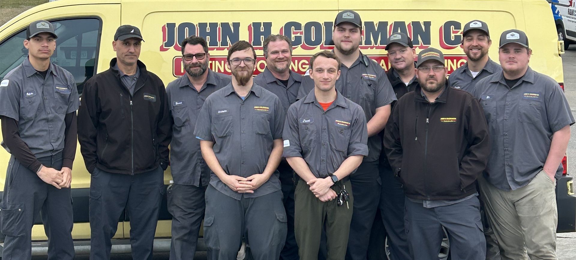 A group of men in work uniforms stand in front of a yellow van with company logo.
