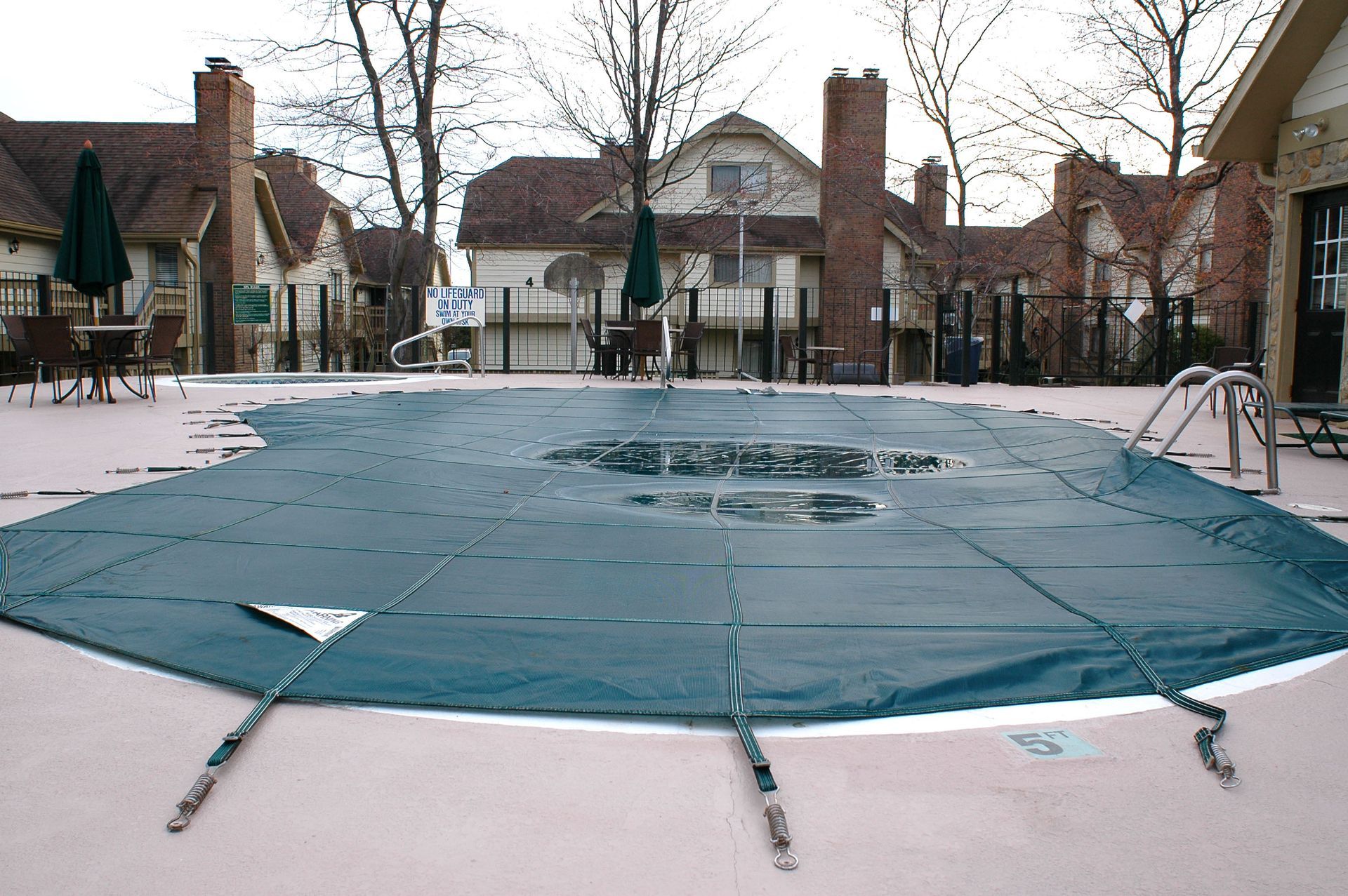 A green pool cover on a closed outdoor swimming pool, with buildings in the background.