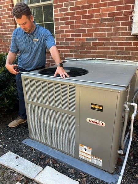 Man in blue shirt measures the top of a Lennox air conditioning unit next to a brick building.