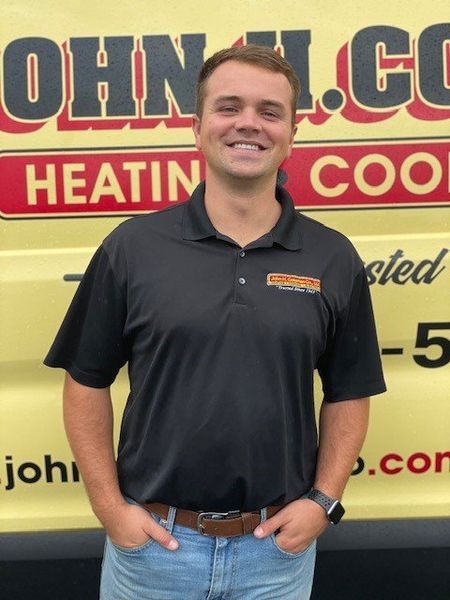 Man in black polo shirt smiles, standing in front of a yellow vehicle with company logo: 