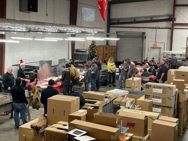 Warehouse Christmas party with people, tables, boxes, and a tree.