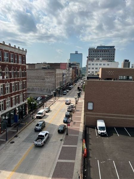 Street view of a city with cars, buildings, and a cloudy sky.
