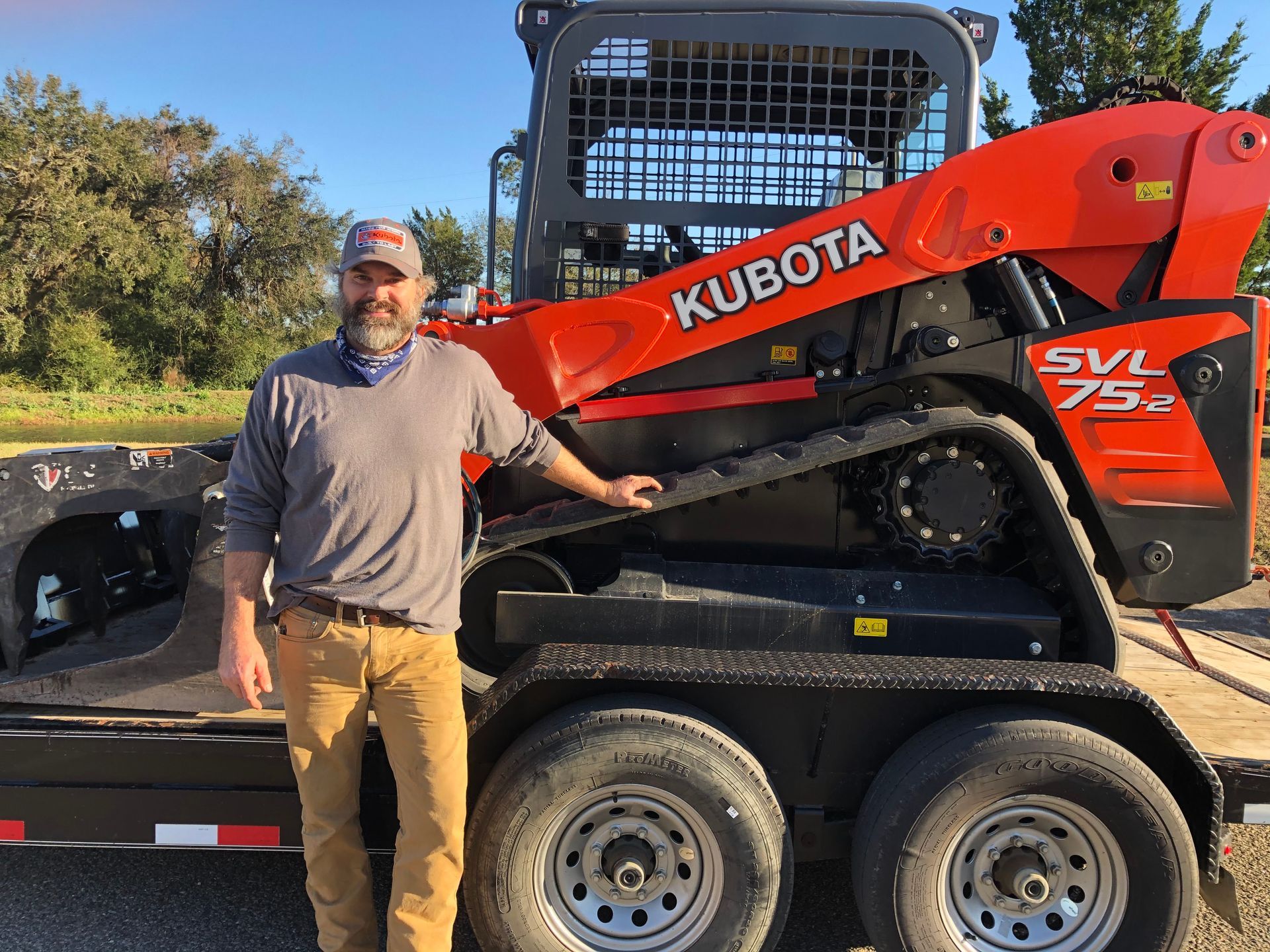A man is standing next to a kubota skid steer on a trailer.
