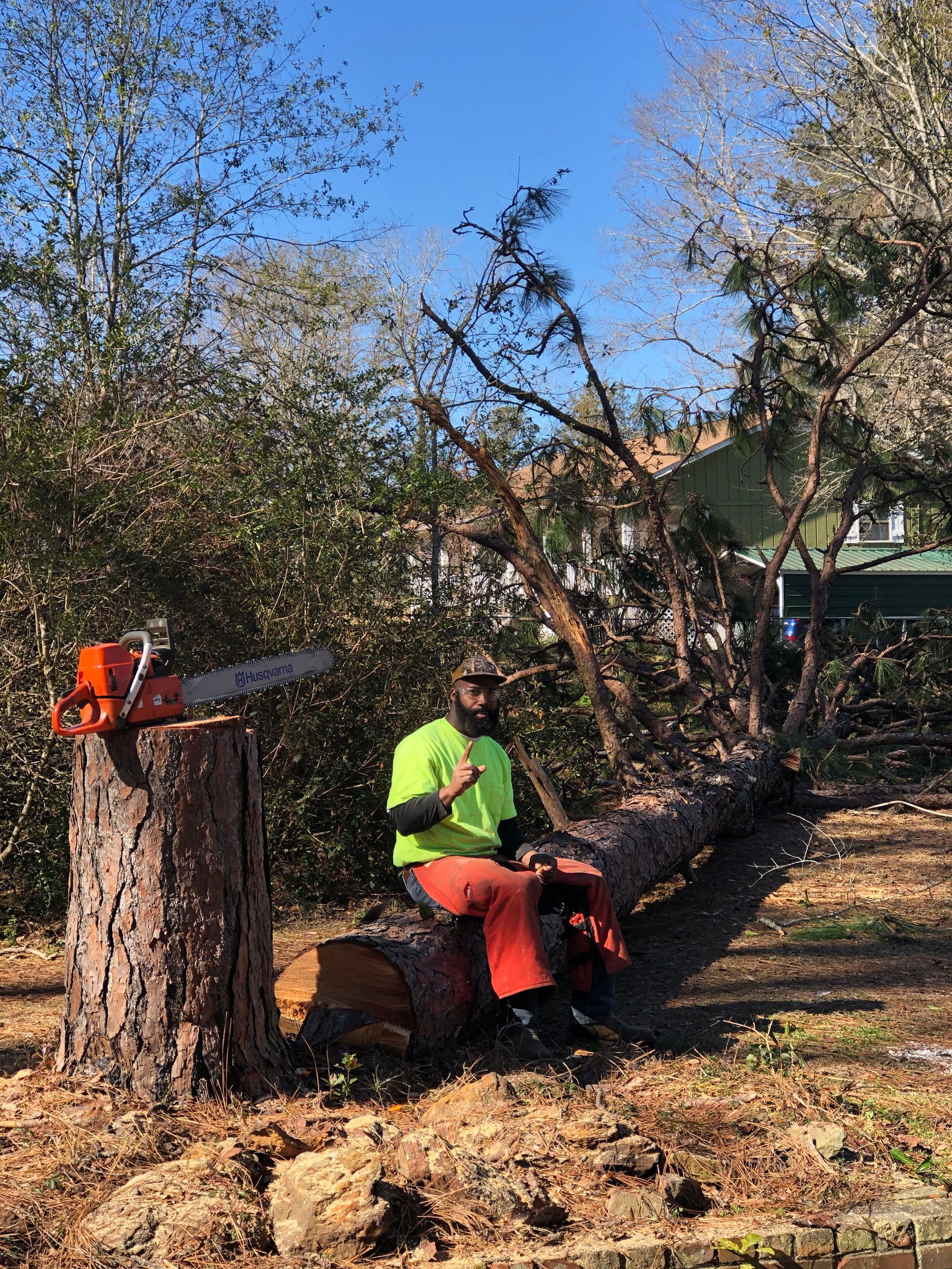 A man is sitting on a tree stump next to a chainsaw.