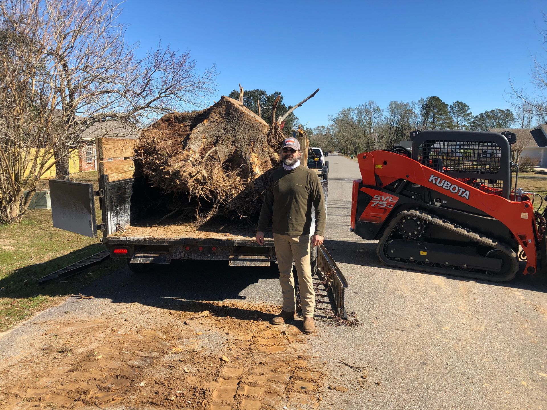 A man is standing next to a bulldozer carrying a large tree stump.