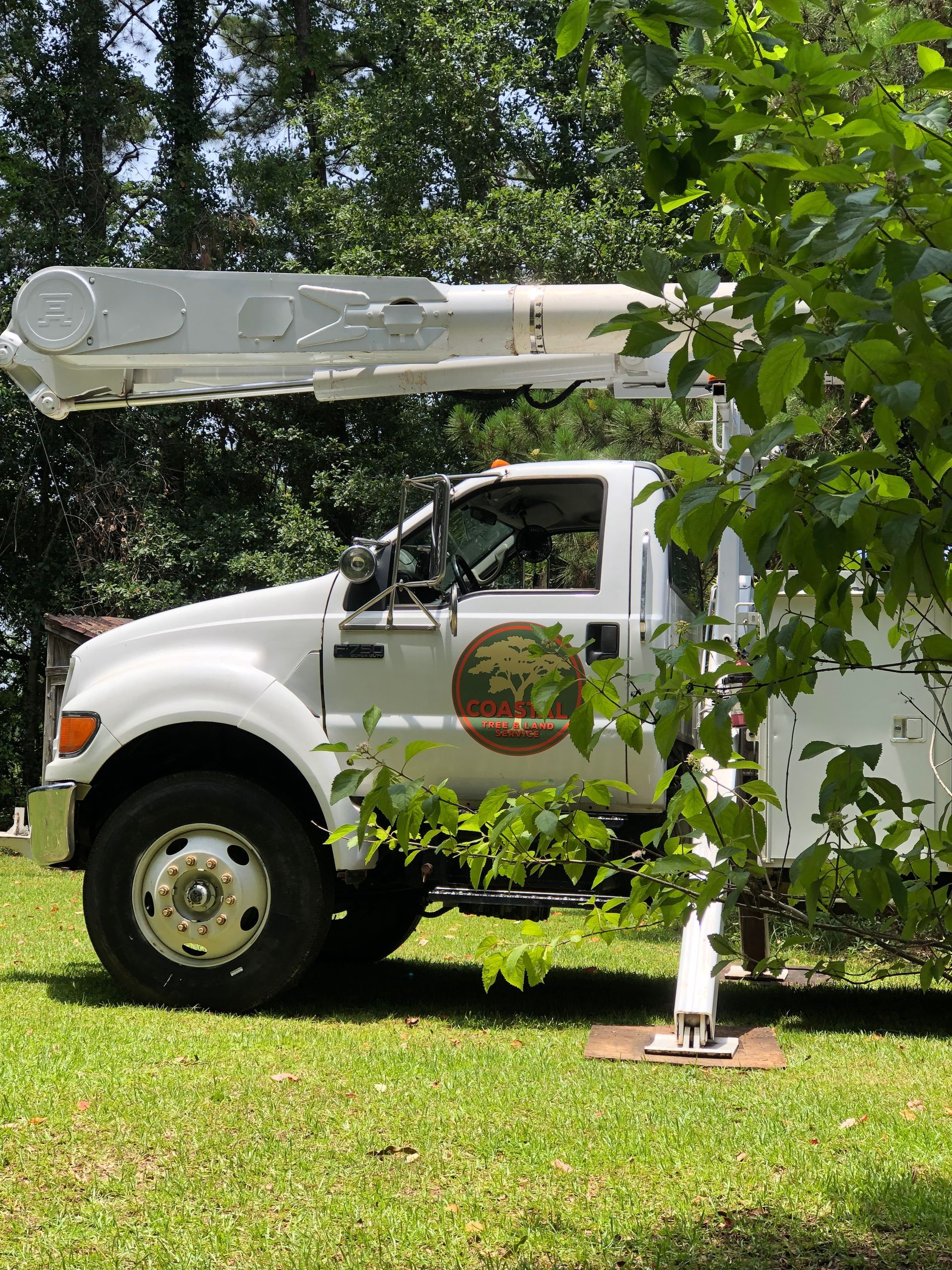 A white truck with a crane on top of it is parked in a grassy field.