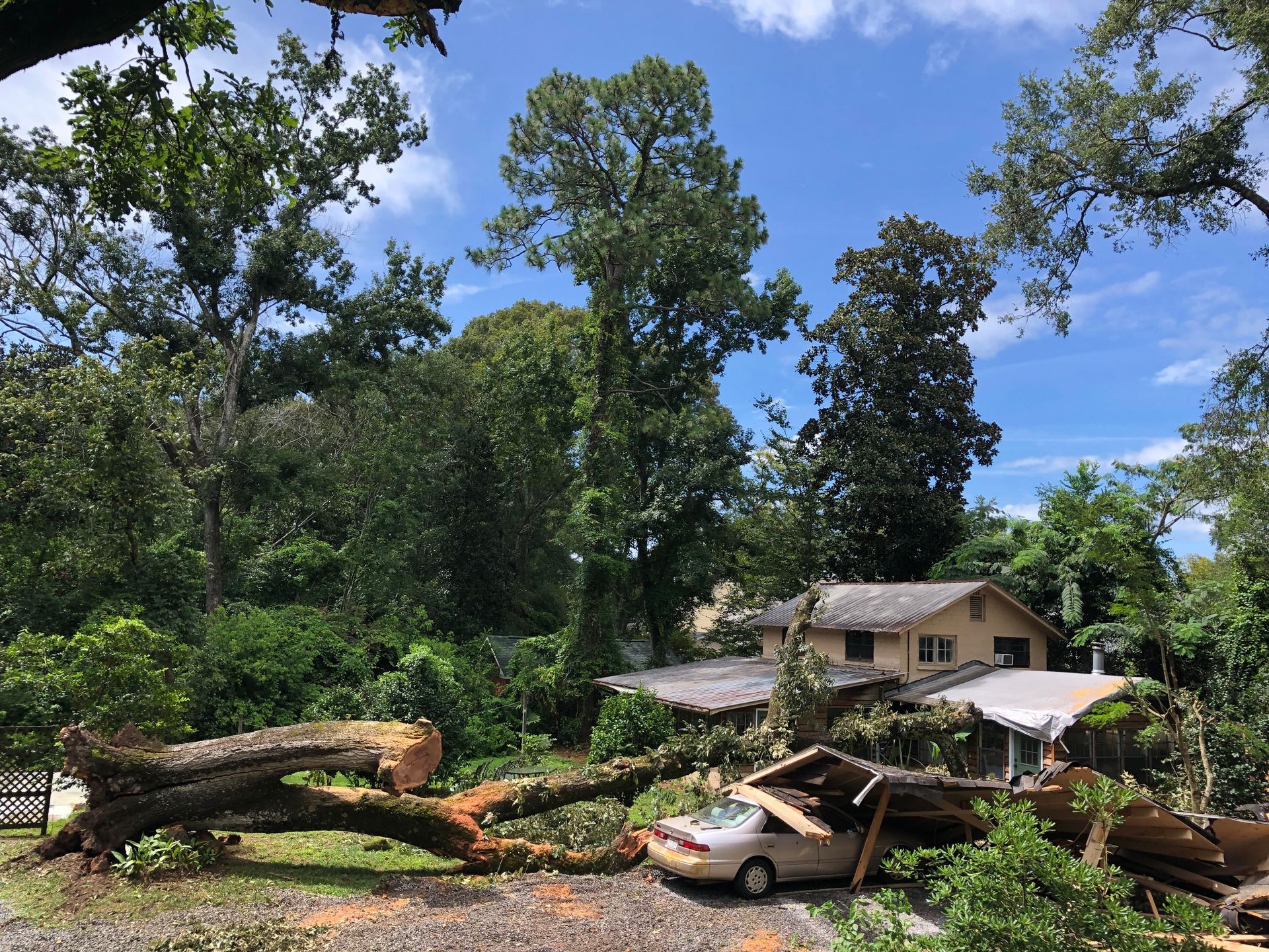 A car is parked in front of a house that has been damaged by a tree.
