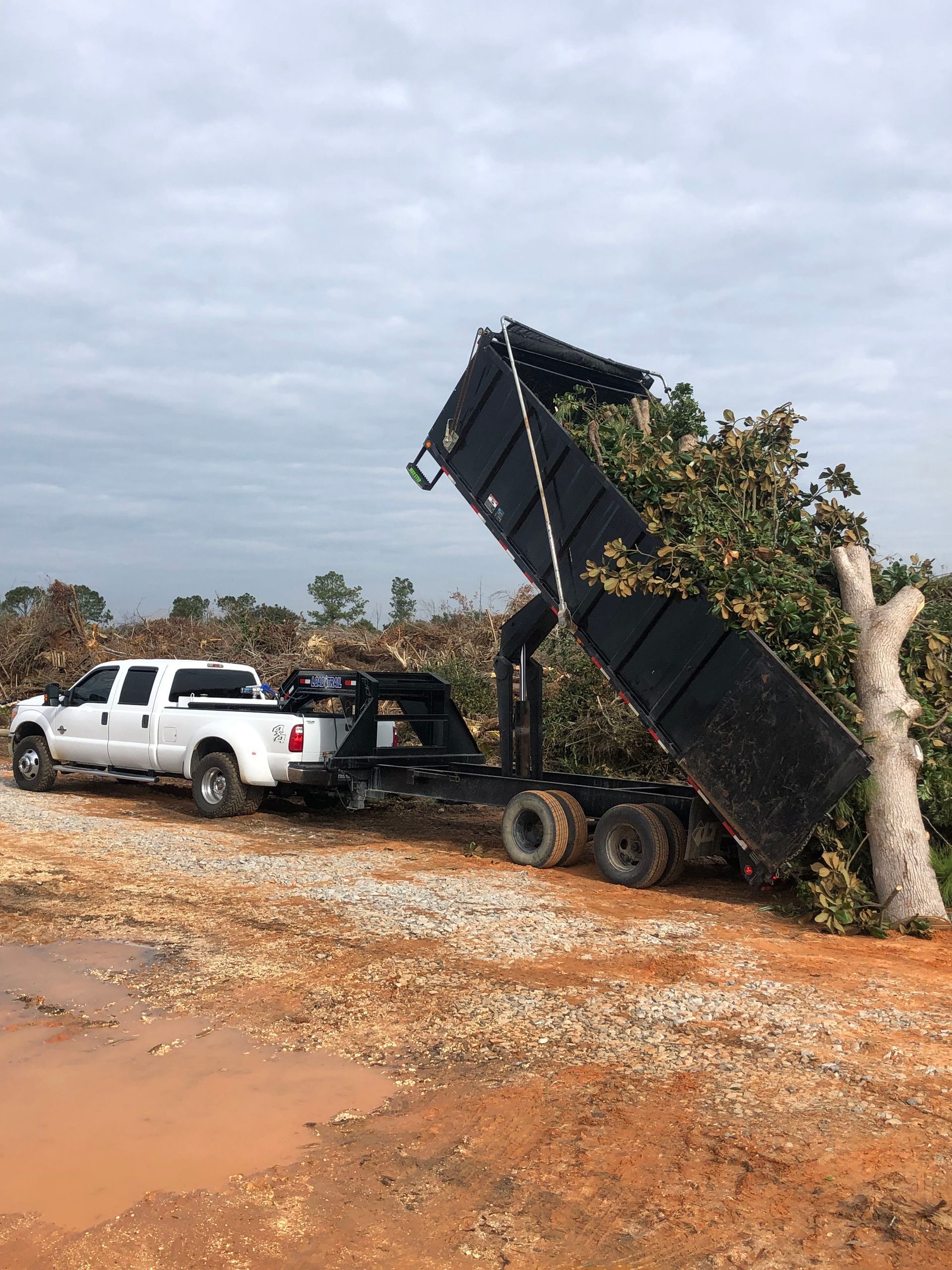 A white truck is being towed by a dump truck.