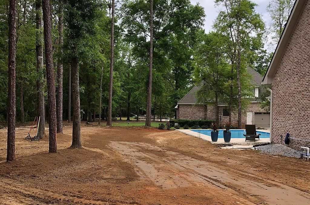 A house with a pool in the backyard is surrounded by trees and dirt.