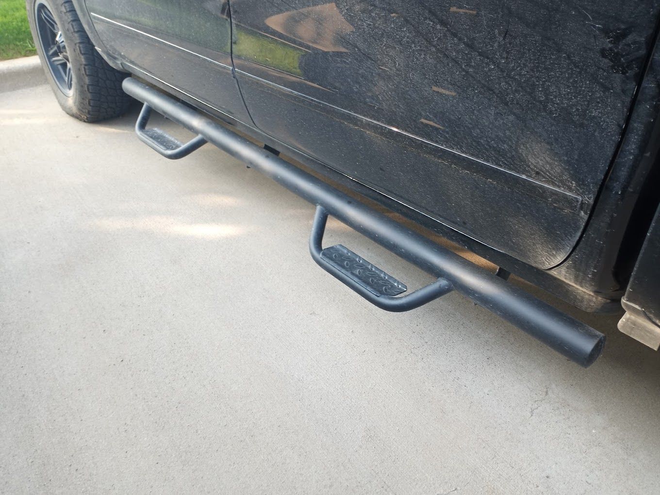 A black truck with side steps is parked in a driveway.