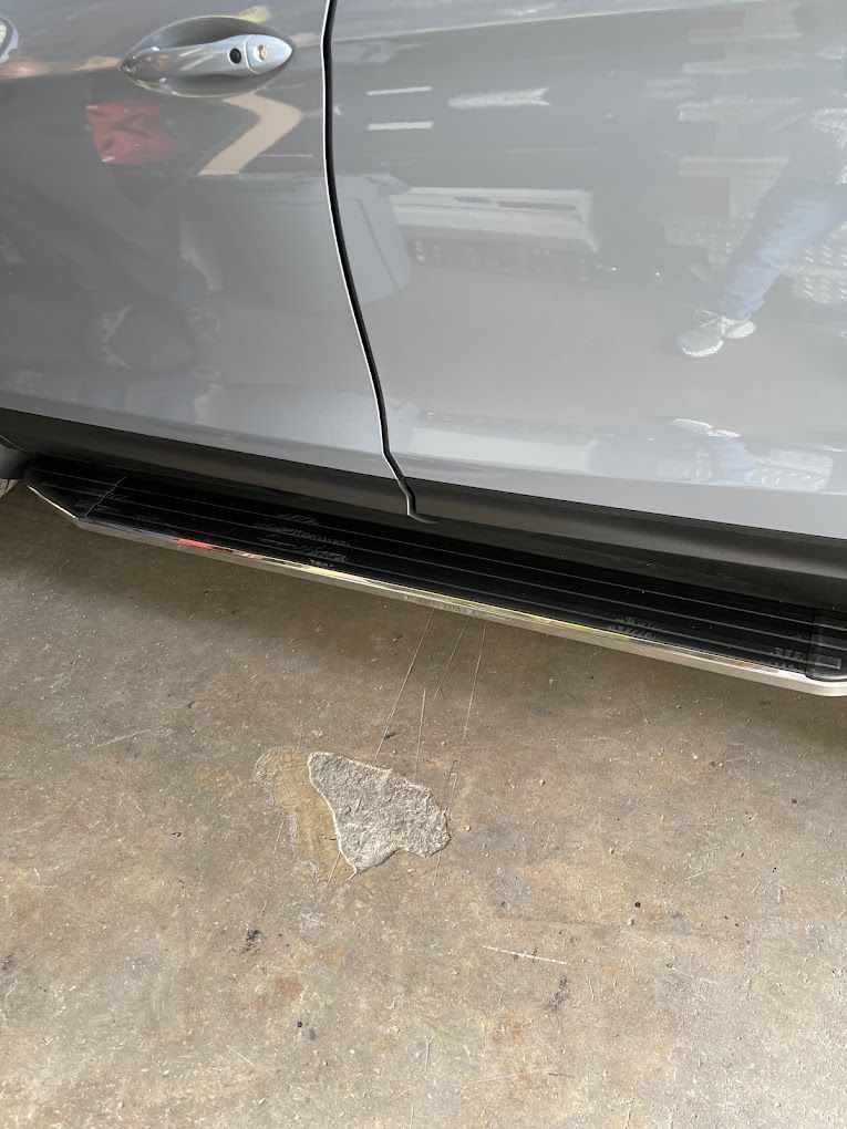A gray car with side steps is parked in a garage.