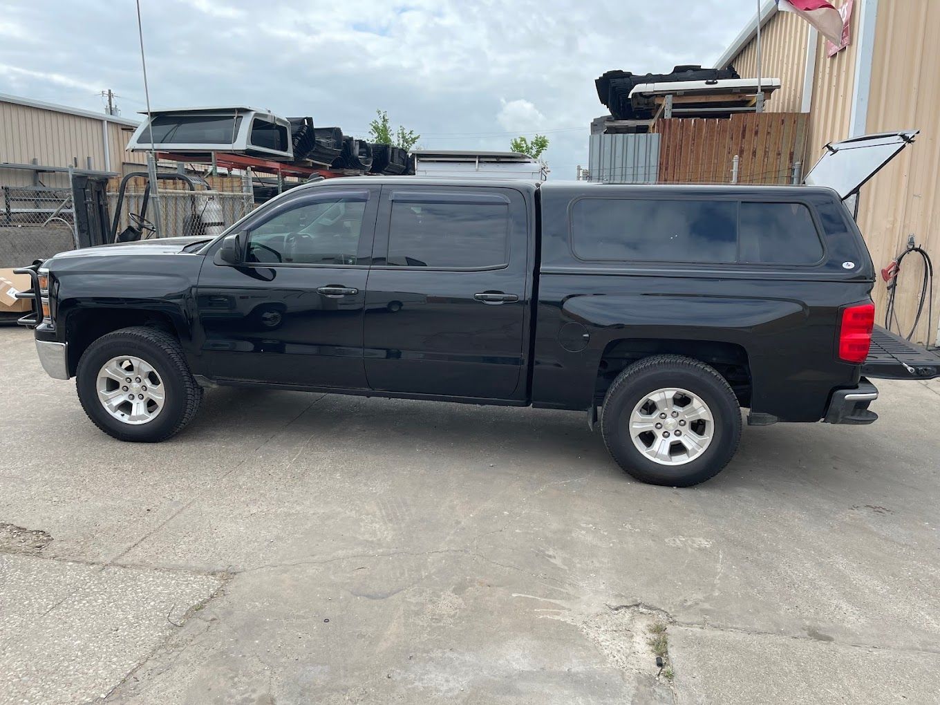 A black truck with a canopy on top of it is parked in front of a building.