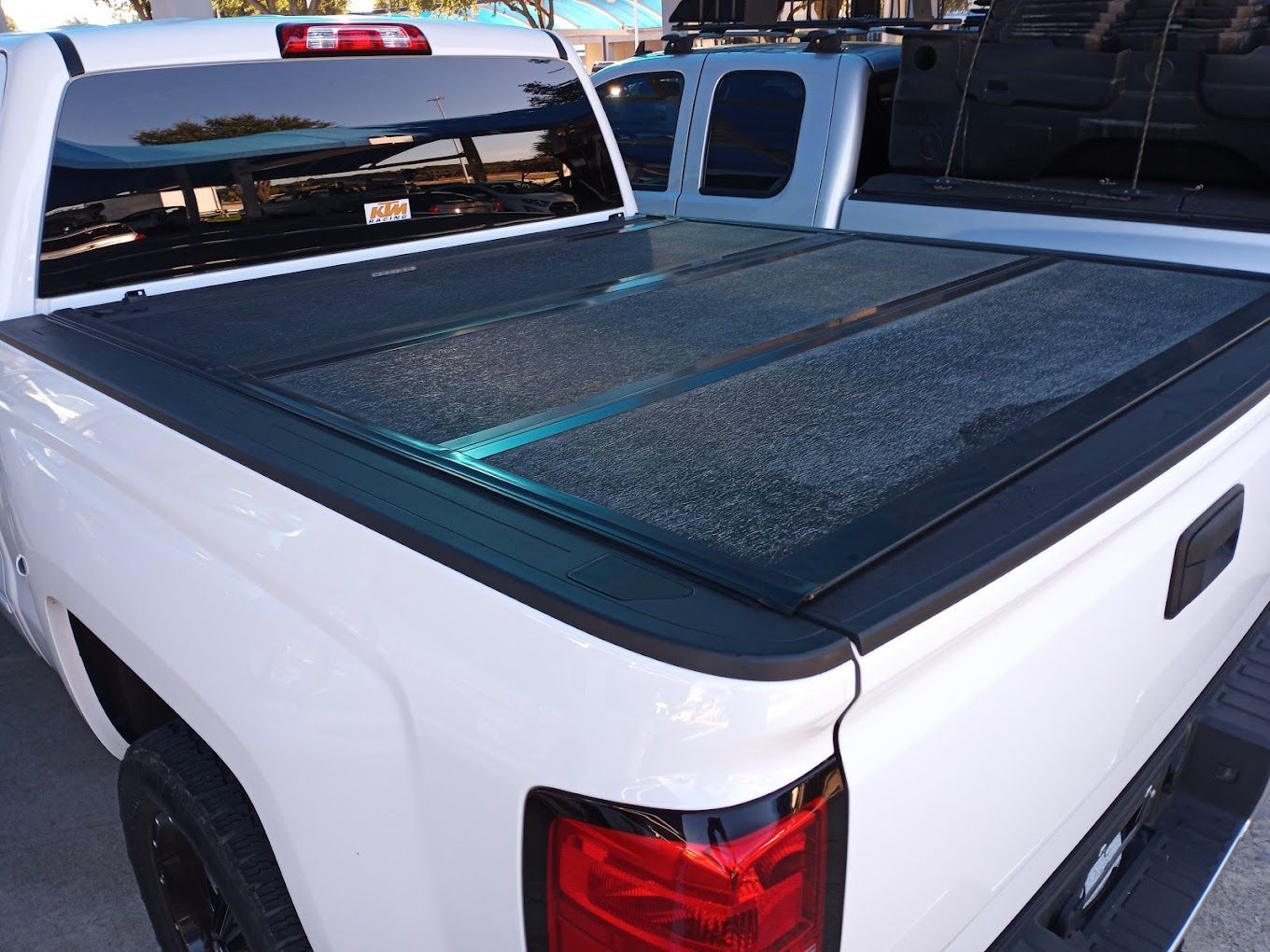 A white truck with a black bed cover is parked on the side of the road.