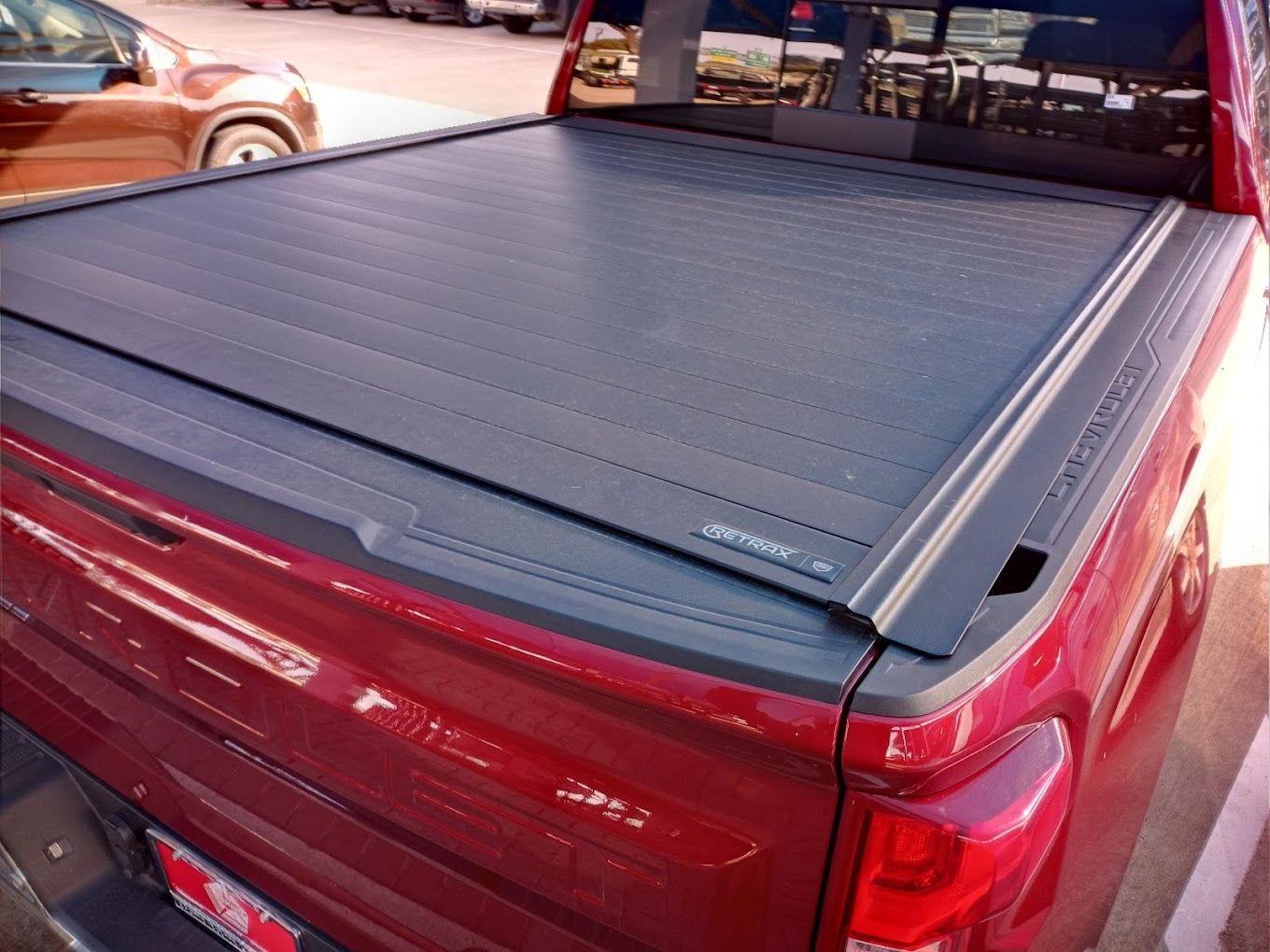 A red truck with a black bed cover is parked in a parking lot.