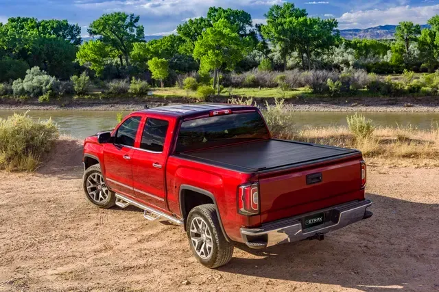 A red truck is parked on a dirt road next to a river.