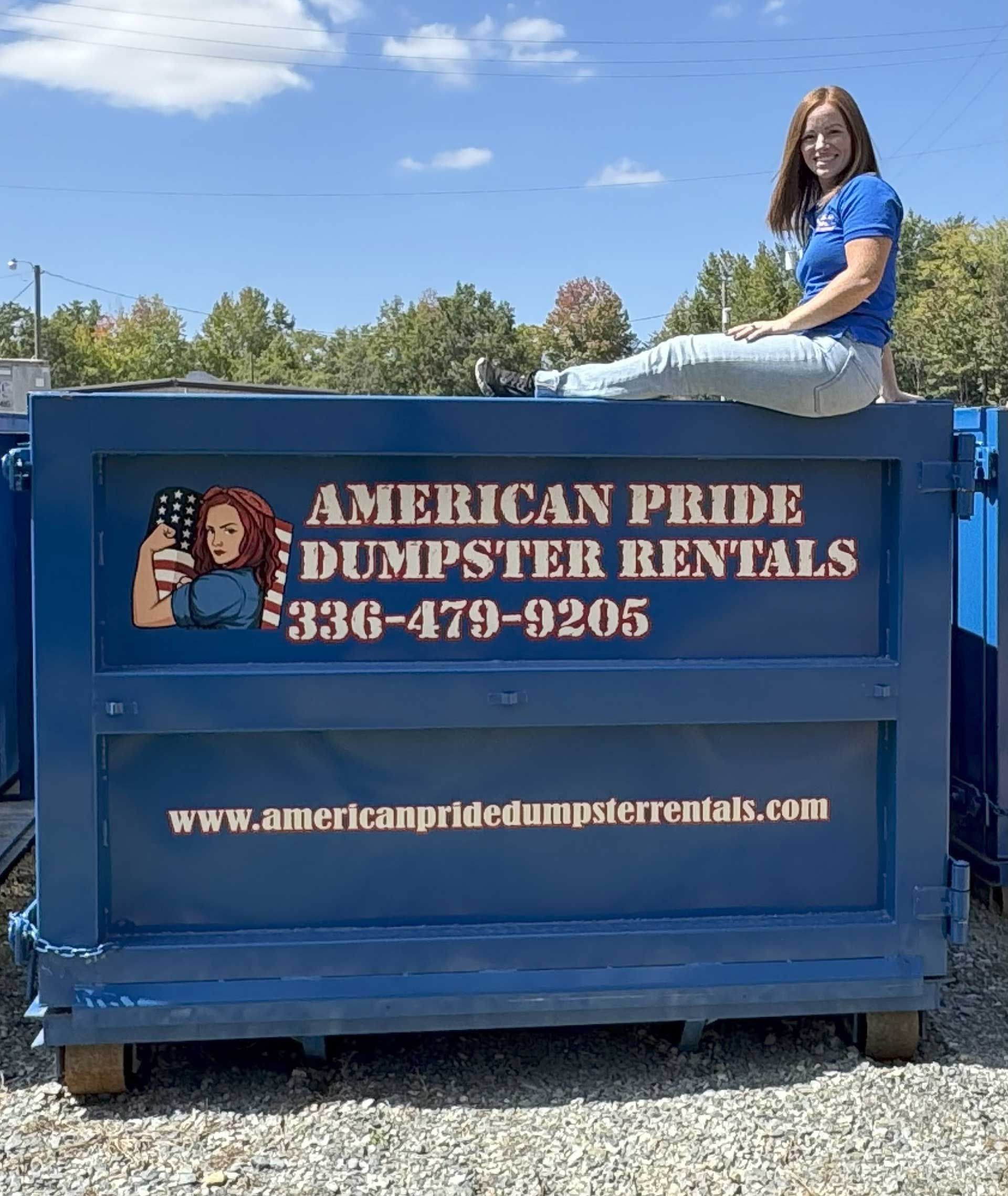 Woman sits on a blue dumpster with "American Pride Dumpster Rentals" logo.