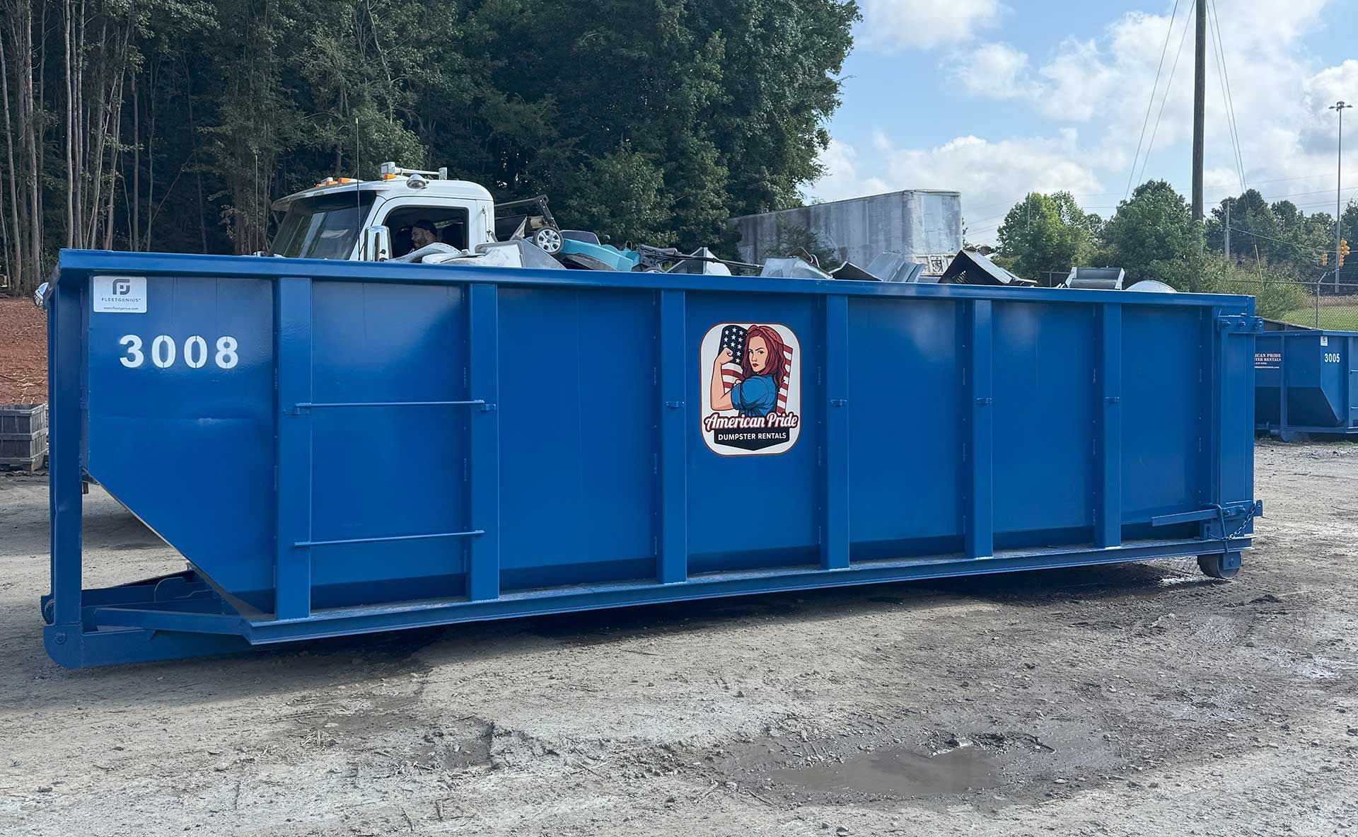 Blue dumpster labeled 3008, filled with trash, on a gray surface. Truck visible in background.
