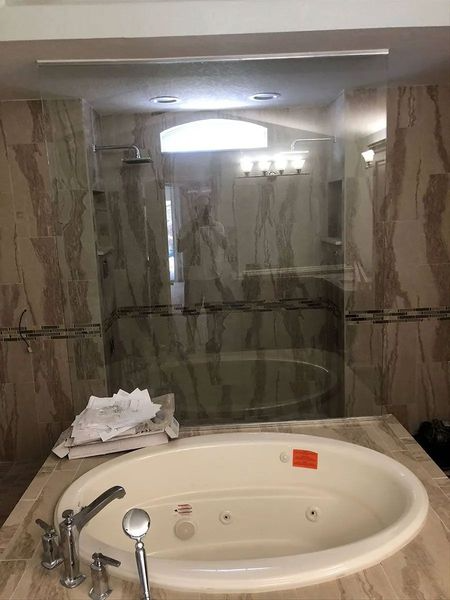 Bathroom with oval jacuzzi tub, glass shower, and marble-look tile walls.
