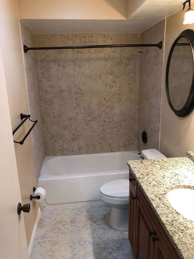 Bathroom with a white bathtub, toilet, and vanity with a granite countertop.