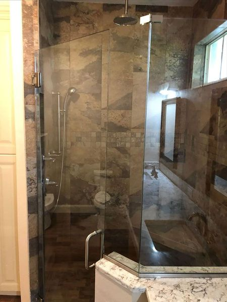 Shower with glass door, brown tile walls, handheld and rain showerheads, a built-in seat, and a vanity reflected in the glass.