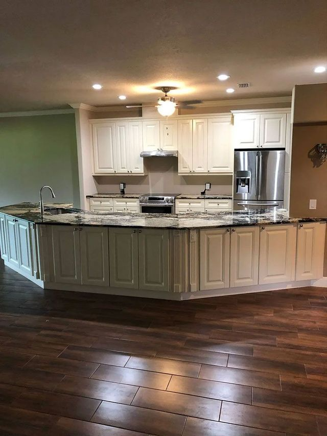 Modern kitchen with white cabinets, granite island, stainless steel appliances, and dark hardwood floors