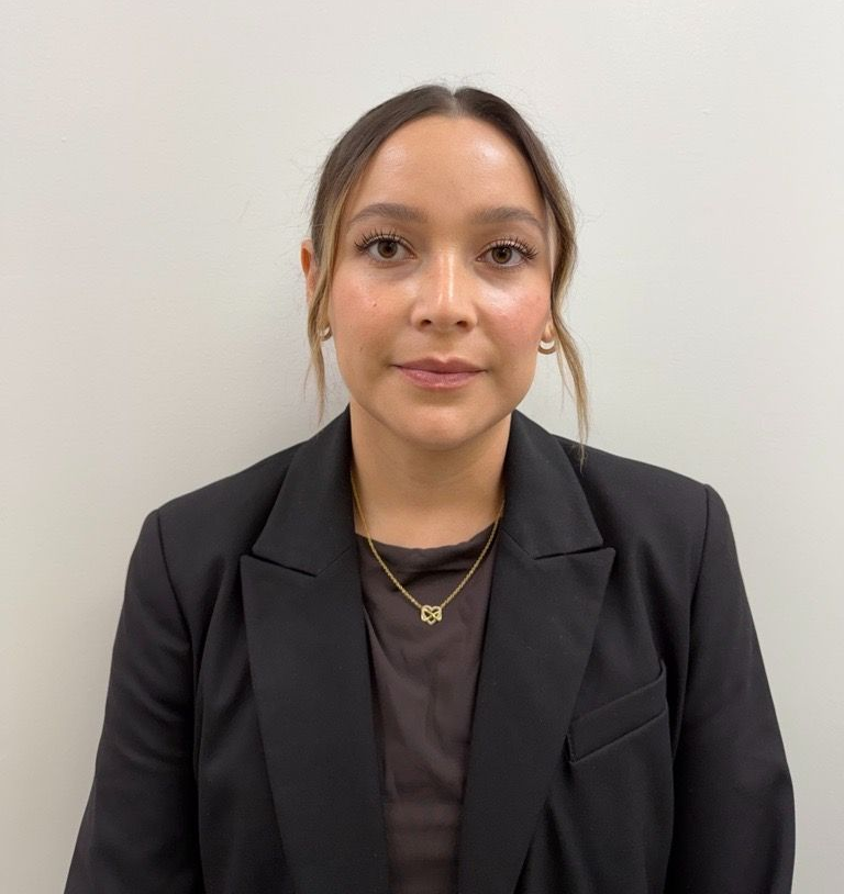 A woman with curly hair is wearing a black shirt and a grey jacket.