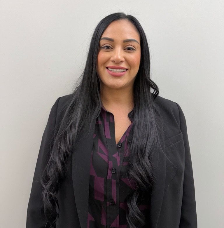 A woman with curly hair is wearing a black shirt and a grey jacket.