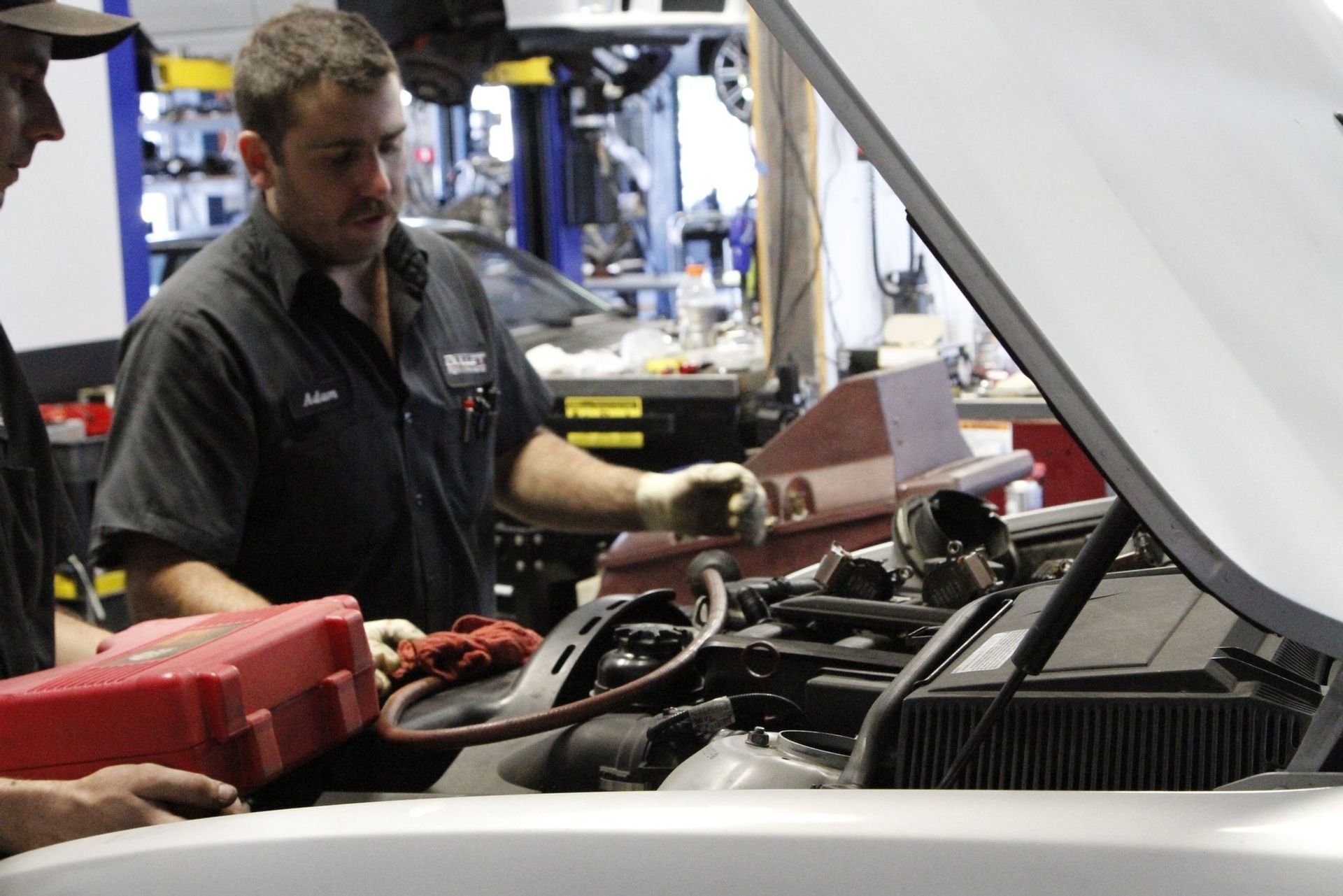 Two men are working on a car with the hood open