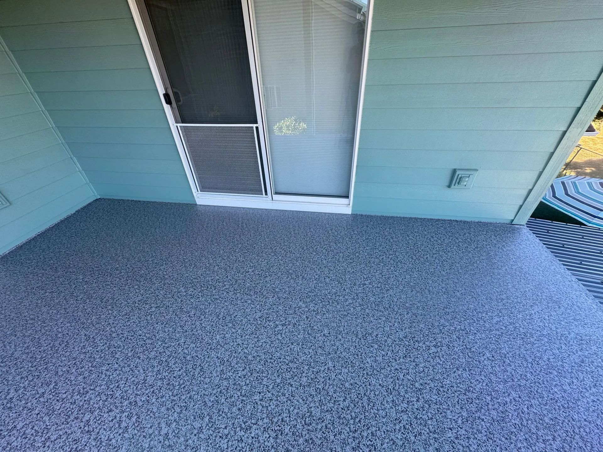 Small screened porch with light blue siding and gray carpeted floor, viewed from an angle.
