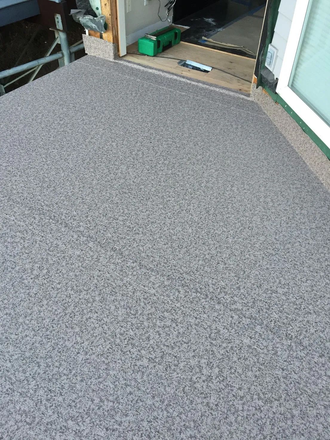 Gray speckled carpeted floor beside a doorway with construction materials and tools nearby