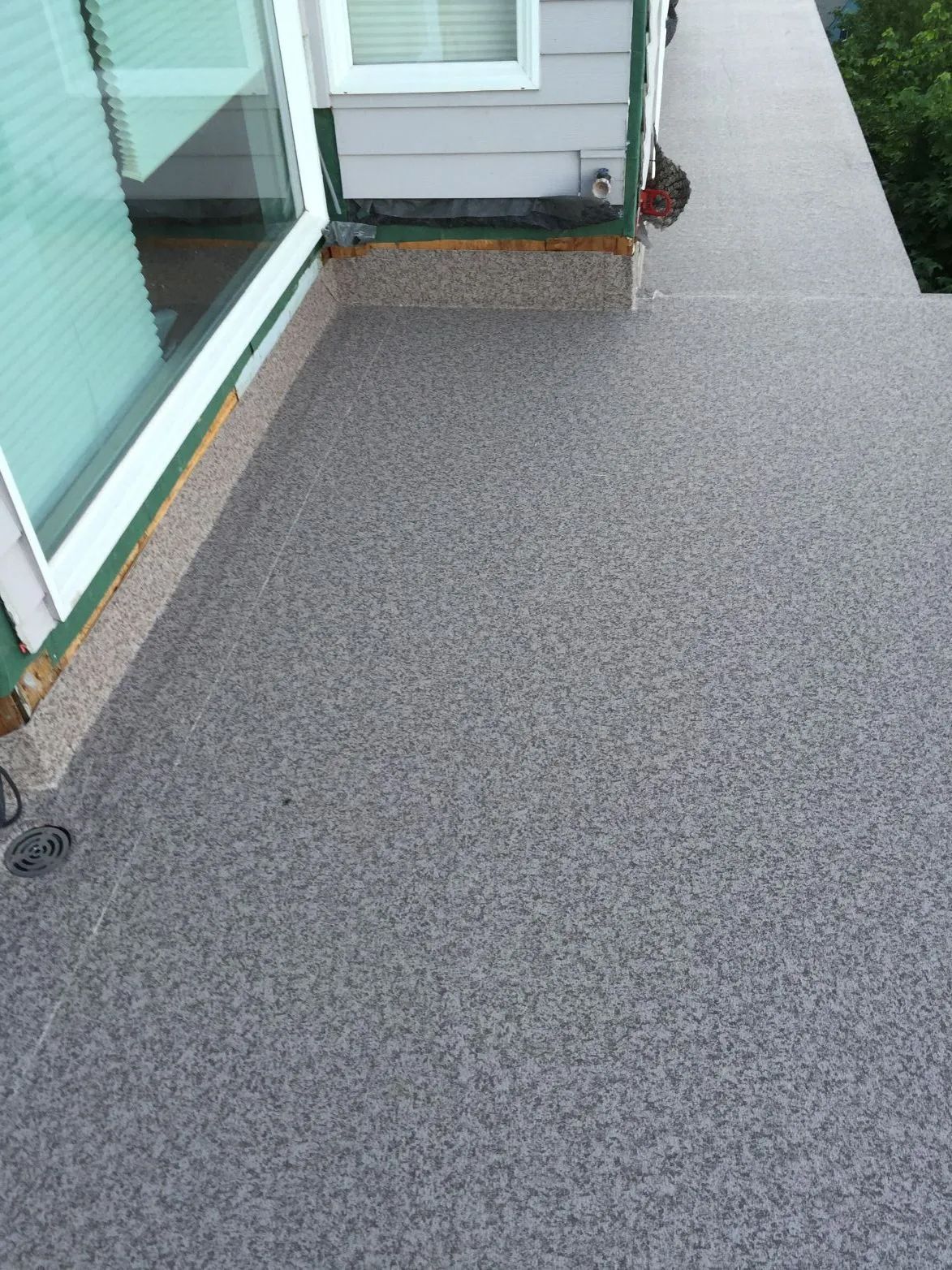 Gray speckled outdoor balcony beside a glass sliding door and white wall trim.