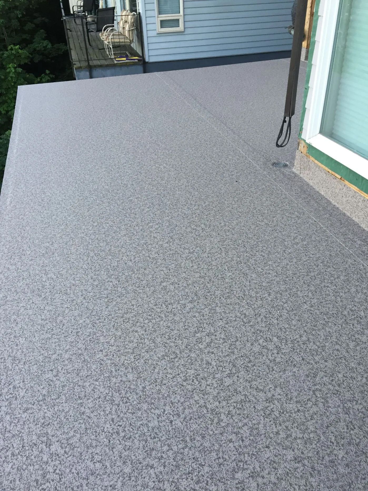 Gray speckled rooftop deck beside a white-sided house and green-trimmed doorframe